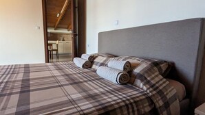 A bedroom with a wooden ceiling, a bed with plaid bedding, and a small bedside table. - Samaras Apartments - Sea View Attic (Kamena Vourla)