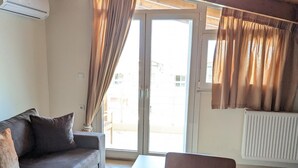 A living room with a sofa, a coffee table, and a chair. There is a sliding glass door leading to an outdoor area. - Samaras Apartments - Sea View Attic (Kamena Vourla)