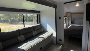 Een modern interieur van een camper met een ingebouwde bank, een bed en een televisie.