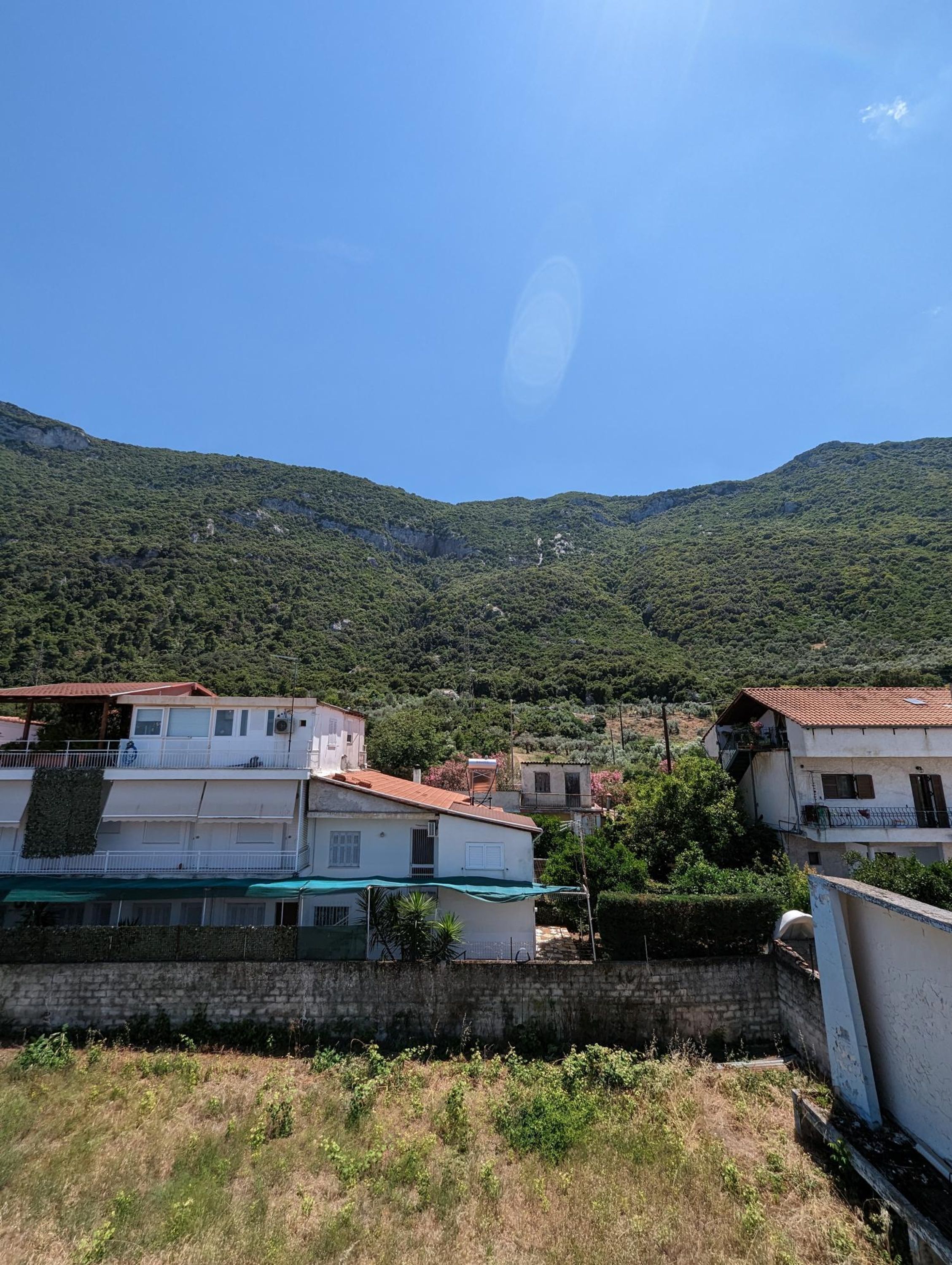 A hillside residential area with buildings, a stone wall, and a clear blue sky.