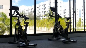 Due cyclette fisse in una stanza con ampie finestre che si affacciano su una zona residenziale.