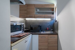 Una cocina compacta con horno empotrado, un lavamanos y armarios de madera.