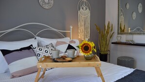 Ein ordentlich bezogenes Bett mit Kissen, ein Tablett mit Tassen und Keksen, eine Vase mit Sonnenblumen und ein Wandbehang aus Makramee.