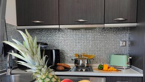 Eine Küche mit dunklen Schränken, einer gefliesten Spritzschutzwand, einer Obstschale mit Ananas, Mango und Banane, einem Toaster und einem Wasserkocher.