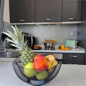 Eine Küche mit dunklen Schränken, einer gefliesten Spritzschutzwand, einer Obstschale mit Ananas, Mango und Banane, einem Toaster und einem Wasserkocher.
