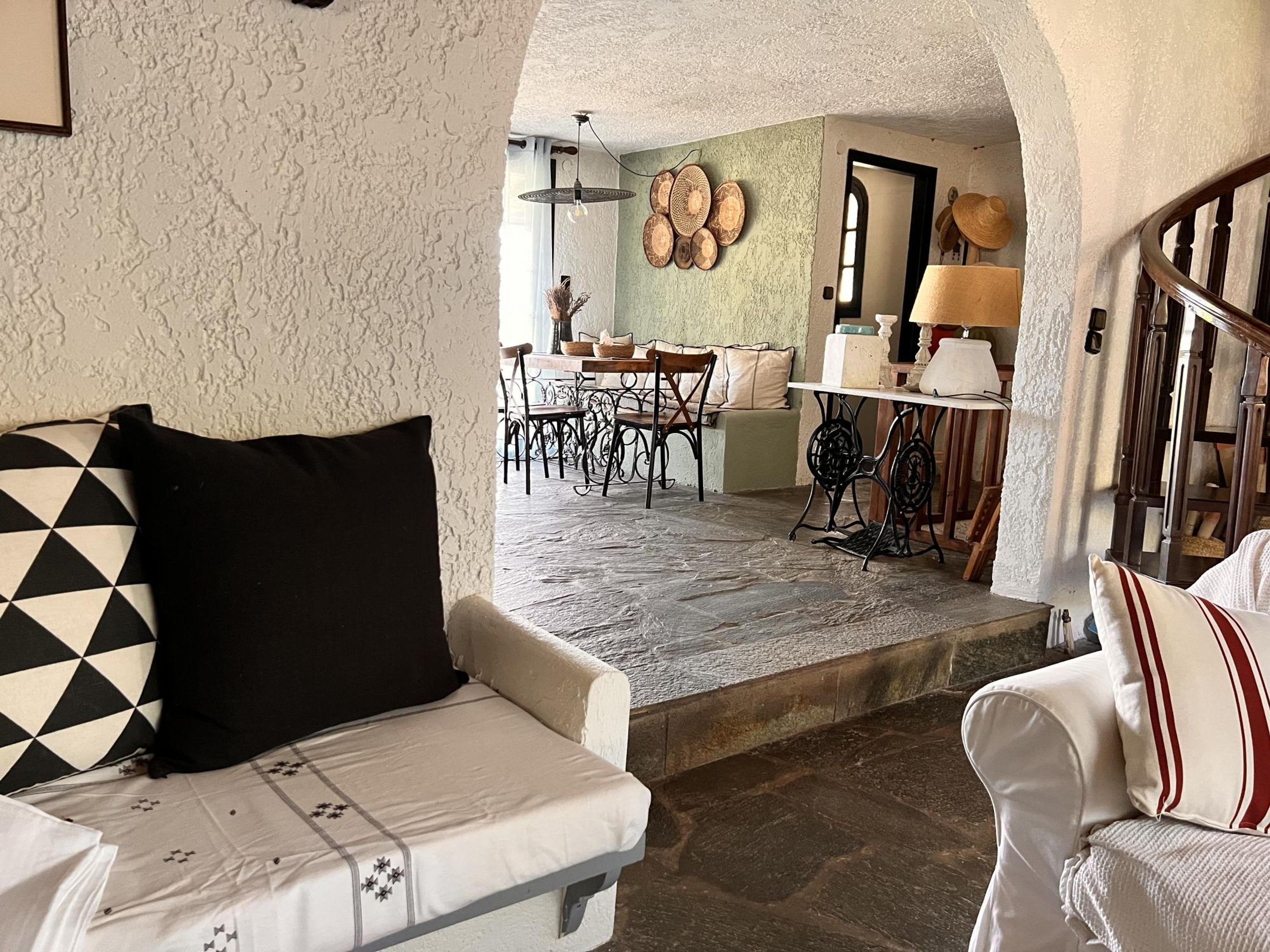 A cozy interior with a white sofa, a dining area with a table and chairs, and a kitchen area with a stove and cabinets.
