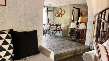 A cozy interior with a white sofa, a dining area with a table and chairs, and a kitchen area with a stove and cabinets.