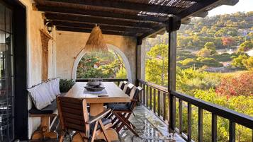 A covered outdoor dining area with a stone floor, wooden furniture, and a view of a lush landscape.