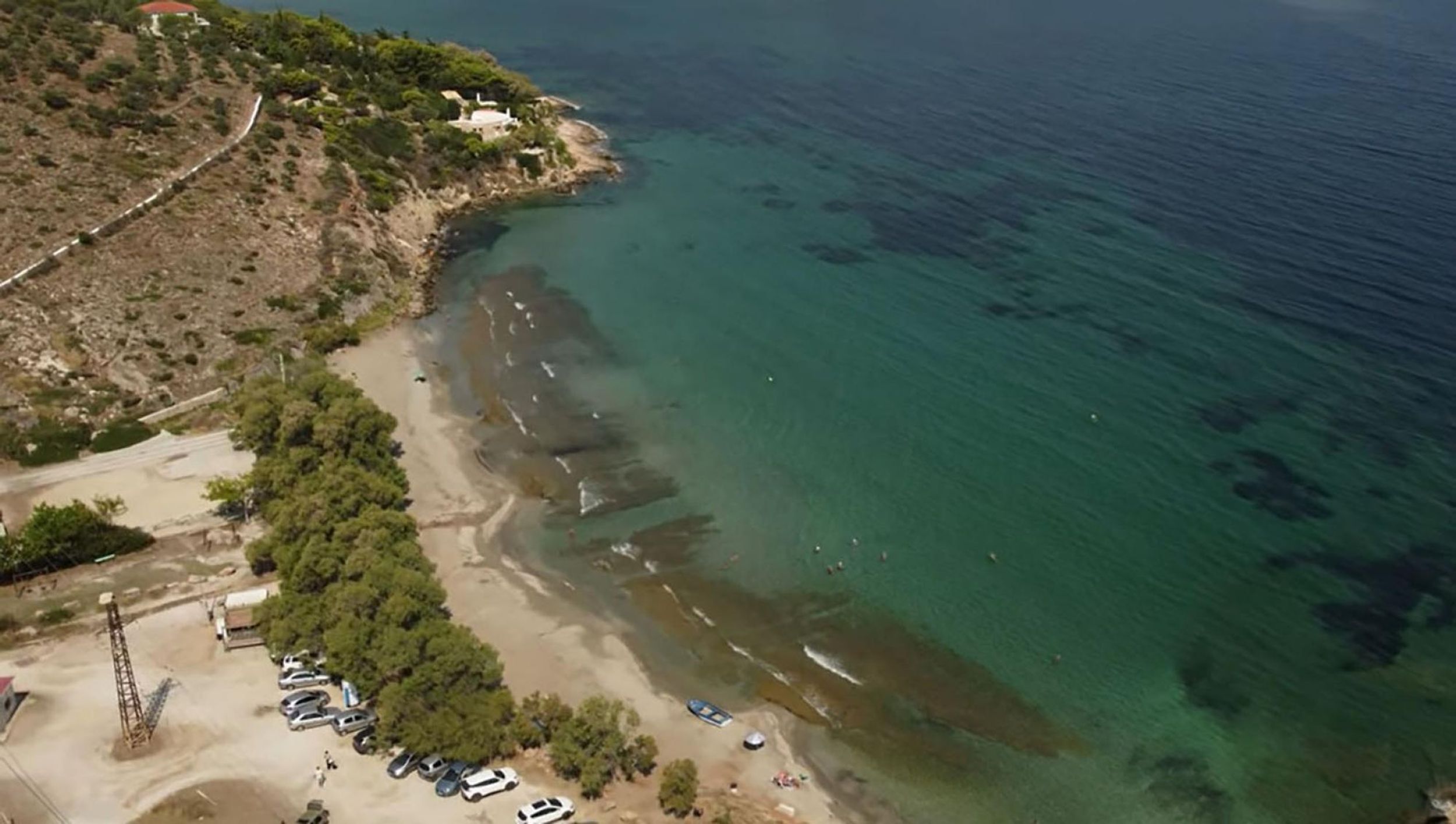 An aerial view of a coastal area with a beach, parked cars, and a small building.