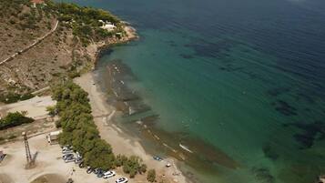 An aerial view of a coastal area with a beach, parked cars, and a small building.