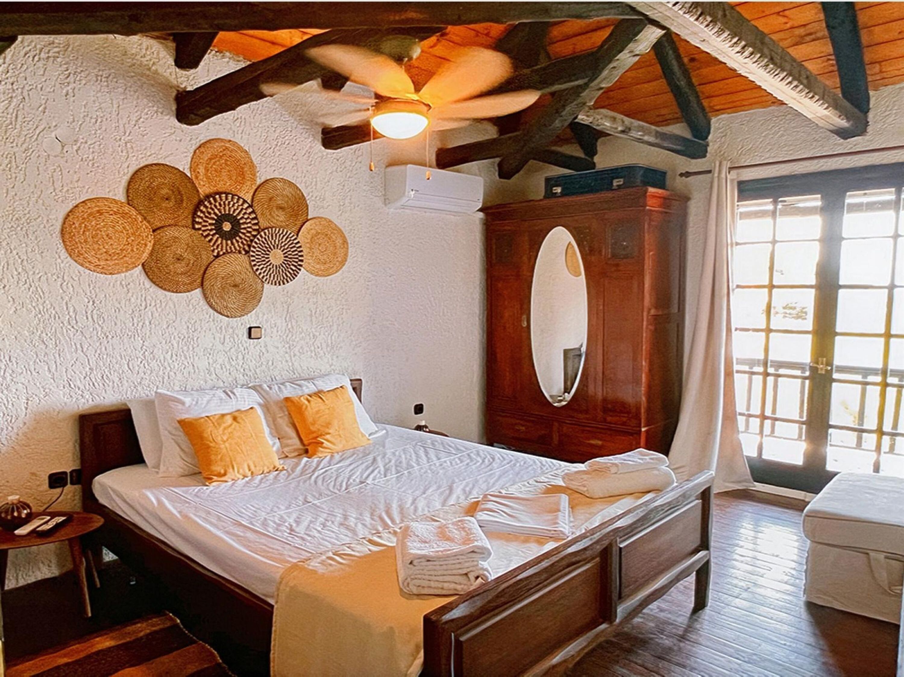 A bedroom with a wooden bed, a ceiling fan, a large mirror, and a wall-mounted woven decoration.