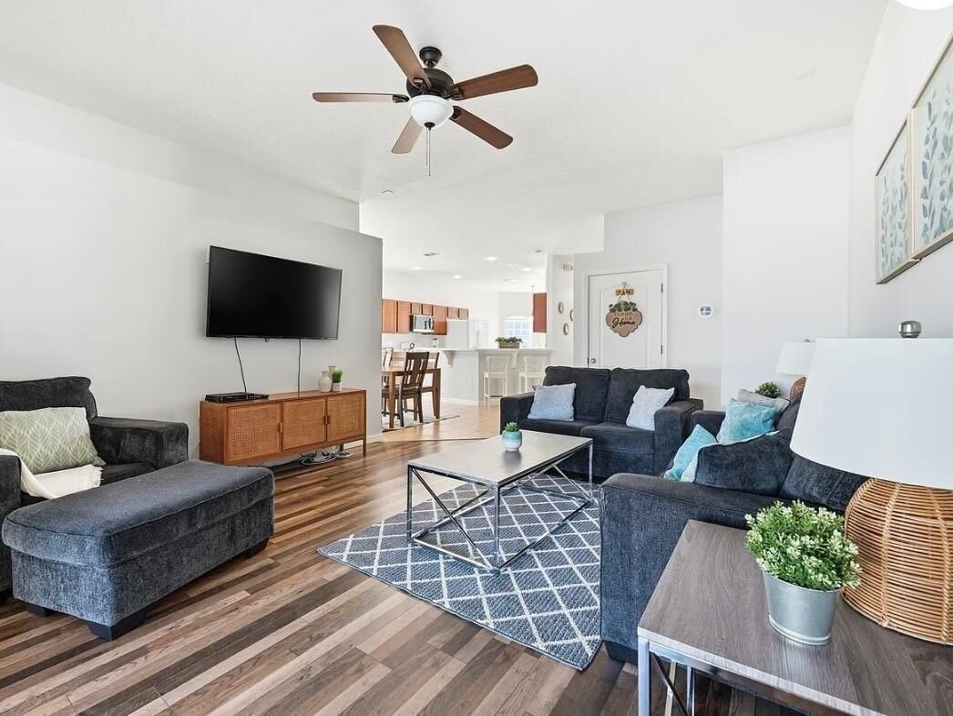 A modern living room with a flat-screen TV, dark sofas, a coffee table, and a ceiling fan.