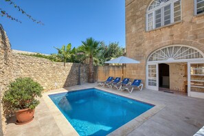 A pool area with a stone wall, a potted plant, and lounge chairs. - Kikka - Xaghra Holiday Home (Ix-Xagħra)