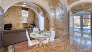 A stone-walled room with a round table set for dining, a sofa, and a television. - Kikka - Xaghra Holiday Home (Ix-Xagħra)