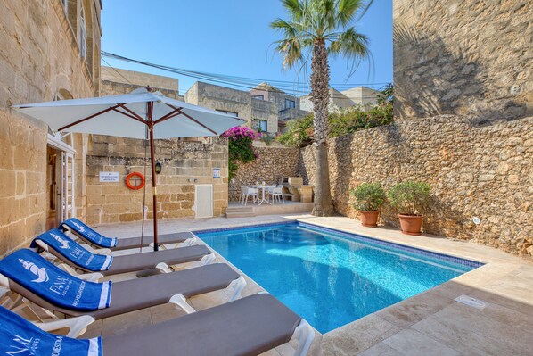 A swimming pool with lounge chairs, a palm tree, and stone walls. - Kikka - Xaghra Holiday Home (Ix-Xagħra)