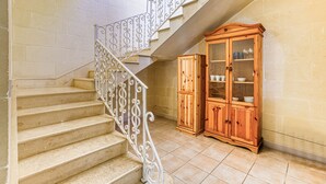 Un escalier avec des rampes blanches richement décorées, un meuble en bois doté de portes en verre et un revêtement de sol en carrelage beige.