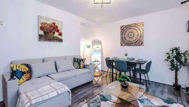 Una sala moderna con un sofá gris, una mesa de centro de vidrio y un comedor con una mesa y sillas.