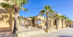 A hotel with a stone facade, palm trees, and a clear blue sky.