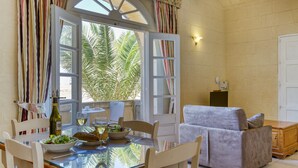A dining area with a glass table, white chairs, a bowl of salad, and a bottle of wine. - Villagg tal-Fanal - 1BDR (L-Għasri)