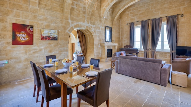 A spacious room with a stone wall, a dining table set with plates and glasses, a sofa, and a fireplace. - Gharilma IV – Santa Lucija Holiday Home (Ta' Kerċem)