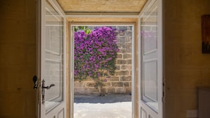 An open doorway leading to a courtyard with a stone wall and a flowering plant. - Gharilma IV – Santa Lucija Holiday Home (Ta' Kerċem)