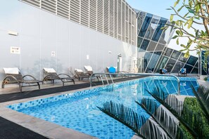 A modern pool area with lounge chairs and a glass building in the background. - Stayshort - Modern 1BR in Business Bay for 2 (Dubai)