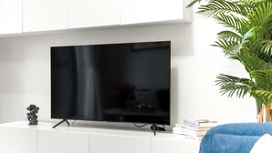 Un salon moderne avec un téléviseur à écran plat posé sur un meuble blanc, un fauteuil bleu et une plante en pot.