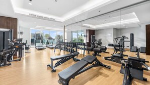 Une salle de sport moderne équipée de divers appareils d’exercice, dotée de grandes fenêtres et d’un plancher en bois.