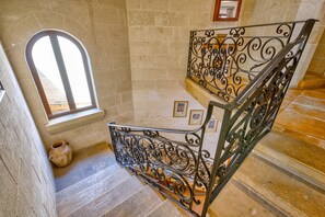 A staircase with ornate metal railings, a stone wall, and a window with natural light. - Gianni - Xewkija Holiday Home (Ix-Xewkija)