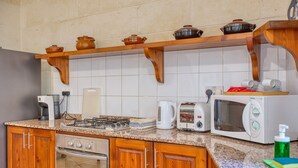 A kitchen with wooden cabinets, a gas stove, a microwave, a toaster, and a coffee maker. - Gianni - Xewkija Holiday Home (Ix-Xewkija)