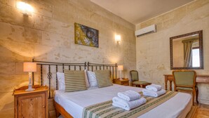 A hotel room with a bed, bedside tables, a mirror, a painting, and an air conditioning unit. - Gianni - Xewkija Holiday Home (Ix-Xewkija)