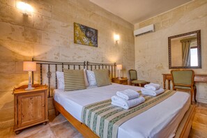 A hotel room with a bed, bedside tables, a mirror, a painting, and an air conditioning unit. - Gianni - Xewkija Holiday Home (Ix-Xewkija)