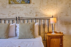 A bed with white bedding and striped pillows, a metal headboard, and a wooden nightstand with a lamp. - Gianni - Xewkija Holiday Home (Ix-Xewkija)