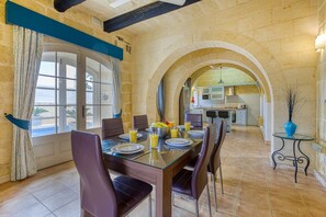 A dining area with a glass table, chairs, and a view of the kitchen through an archway.