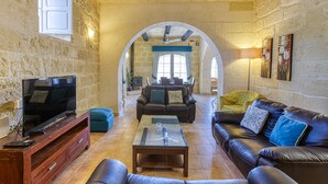 A living room with a stone wall, a television, leather sofas, and a coffee table. - Girardu - Victoria Holiday Home (Victoria)