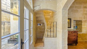 A stone-walled hallway with a staircase, a wooden dresser, and a window with a view of the outside. - Girardu - Victoria Holiday Home (Victoria)