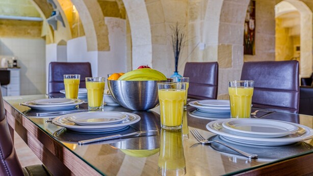 A breakfast table set with plates, glasses, and a fruit bowl. - Girardu - Victoria Holiday Home (Victoria)