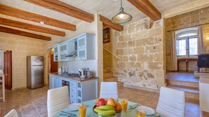Une cuisine spacieuse aux murs en pierre, avec des poutres apparentes et un coin repas où la table est mise pour le petit-déjeuner.