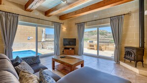 Un salon avec une piscine, des poutres en bois, un téléviseur et une cheminée.