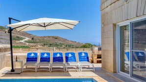Un espace aménagé au bord de la piscine, avec des chaises longues, un parasol et une vue sur un paysage vallonné.