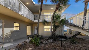 A modern two-story house with a covered patio, a staircase, and a small garden with palm trees and rocks. - Beach Escape with Never Ending Views and Direct Beach Access (Ormond Beach)