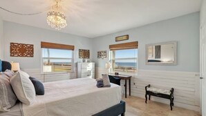 A bedroom with a large bed, a desk, a chair, and a view of the beach. - Beach Escape with Never Ending Views and Direct Beach Access (Ormond Beach)