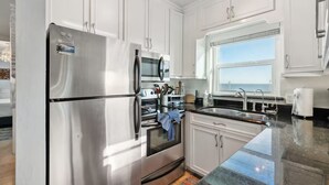 A modern kitchen with stainless steel appliances, white cabinetry, and a large window offering a view of the sea. - Beach Escape with Never Ending Views and Direct Beach Access (Ormond Beach)