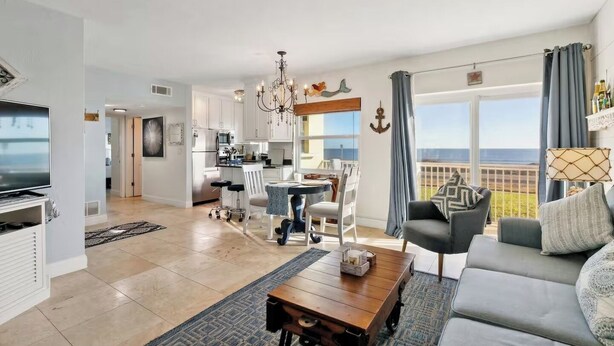 A spacious living area with a dining table, sofa, and kitchen in the background. - Beach Escape with Never Ending Views and Direct Beach Access (Ormond Beach)