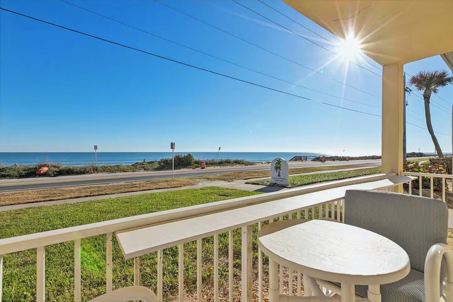 Un balcone con vista sulla spiaggia e sull'oceano, un cartello che indica il luogo, e un'area pranzo con tavolo e sedie.