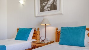 Hotellihuoneessa on kaksi sänkyä, joissa kummassakin on puinen pääty ja valkoiset vuodevaatteet sekä siniset tyynyt. Sänkyjen välissä on yöpöytä, jossa on lamppu.
