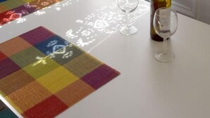A dining table with a colorful table runner, two wine glasses, and a bottle of wine. - Amberi, Tinos in Panormos (Panormos)