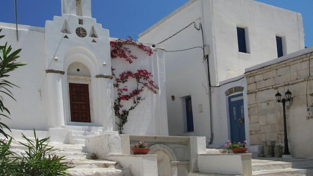 A white building with a bell tower, a blue door, and steps leading to the entrance. - Amberi, Tinos in Panormos (Panormos)