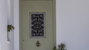 Een lichtgroene deur met een decoratief glasraam, een kleine potplant aan de linkerkant en een witte metalen stoel op de voorgrond.