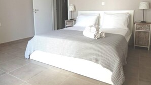 Een net opgemaakt bed met een wit en grijs geruit beddegoed, twee nachtkastjes met lampen, en een deur die naar een andere kamer leidt.